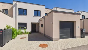 Moderne Reihenhausfassade mit integrierter Garage und gepflasterter Einfahrt unter blauem Himmel.