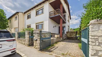Mehrstöckiges Wohnhaus mit Balkonen, gepflasterter Einfahrt und Steinmauer.
