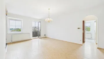 Helles, leeres Wohnzimmer mit Laminatboden und Zugang zu einem französischen Balkon.