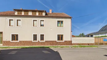 Fassade eines Mehrfamilienhauses mit braunen Fensterrahmen und einem Dachgeschossausbau unter blauem Himmel.