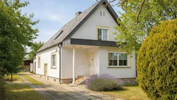 Weißes Einfamilienhaus mit Satteldach, gepflasterter Auffahrt und gepflegter Gartenanlage.