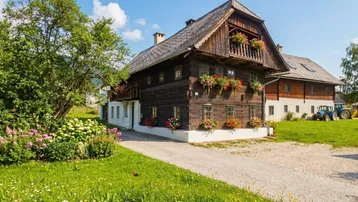 Traditionelles Holzhaus mit Blumenkästen und gepflegtem Vorgarten in ländlicher Umgebung.