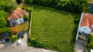 Luftaufnahme eines grünen Baugrundstücks in einer ruhigen Wohngegend mit umliegenden Häusern und viel Grün.
