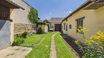 Langer, schmaler Gartenbereich zwischen Gebäuden mit Rasen und Pflanzen.