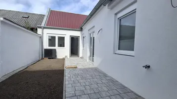 Neubau-Fassade mit gepflasterter Terrasse und vorbereitetem Gartenbereich, ideal für entspannte Stunden im Freien.