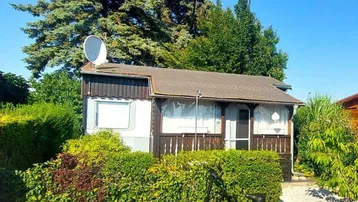 Kleines Haus mit Satellitenschüssel und gepflegter Hecke im Grünen unter blauem Himmel.