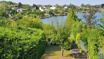 Gepflegter Gartenbereich mit üppigem Grün und direktem Blick auf den See unter blauem Himmel.