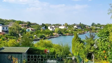 Weitläufiger Gartenbereich mit Rasenfläche, Gartenhaus und Panoramablick auf den See.