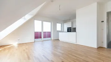Heller Wohnbereich mit Holzboden, Dachschrägen und Zugang zu einem Balkon.