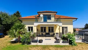 Geräumige Terrasse mit Gartenmöbeln und Zugang zum Garten, ergänzt durch einen Balkon im Obergeschoss.