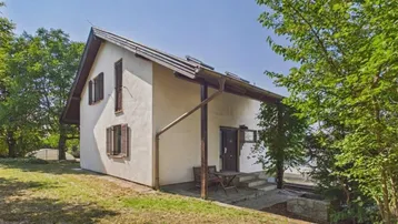 Helles Einfamilienhaus mit Satteldach und Holzfensterläden, umgeben von viel Grün.