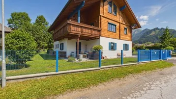 Charmantes Holzhaus im Chalet-Stil mit Balkon und blauen Fensterläden, umgeben von einem gepflegten Garten und Bergblick.