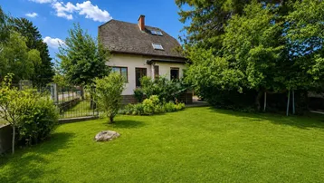 Freistehendes Einfamilienhaus mit großem, gepflegtem Rasen und umgebenden Bäumen unter blauem Himmel.