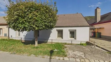 Einfaches Einfamilienhaus mit gepflegtem Vorgarten und ländlichem Charme unter blauem Himmel.