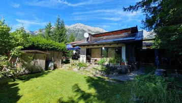 Weitläufiger Gartenbereich mit Rasenfläche und Blick auf die umliegenden Berge unter strahlend blauem Himmel.
