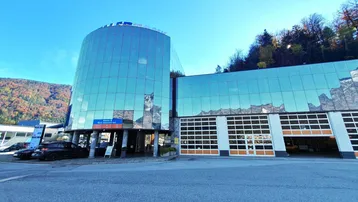 Modernes Geschäftsgebäude mit Glasfassade und Garagentoren, umgeben von Bergen und Parkplätzen.