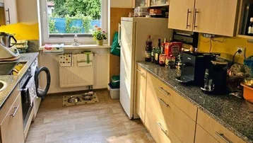 Helle Küche mit Holzschränken, Granitarbeitsplatte und Blick ins Grüne durch das Fenster.