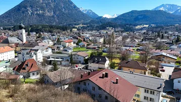 Panoramablick auf die Stadt mit traditionellen Häusern und majestätischen Bergen im Hintergrund.