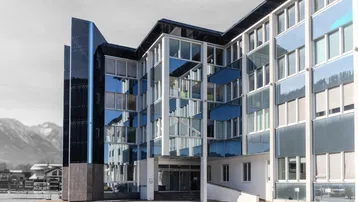 Modernes Gebäude mit Glasfassade und reflektierenden Fenstern vor einer Bergkulisse.