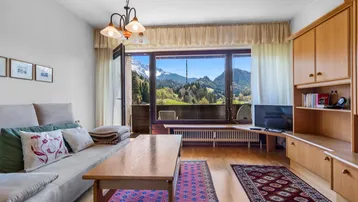 Helles Wohnzimmer mit Holzboden, gemütlichem Sofa und beeindruckendem Bergblick vom Balkon.