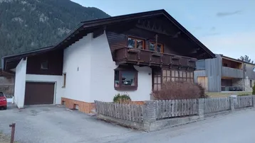 Traditionelles Haus mit Holzbalkonen und weißer Fassade, umgeben von einer ländlichen Landschaft.