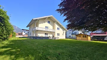 Großzügiger Gartenbereich mit Rasenfläche, Gartenhaus und Blick auf die umliegende Berglandschaft.