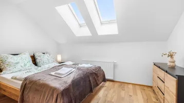 Helles Schlafzimmer im Dachgeschoss mit Holzboden, gemütlichem Bett und zwei Dachfenstern.