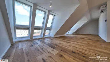 Geräumiger Dachgeschossraum mit großen Fenstern, Holzboden und Klimaanlage, ideal für Wohnzwecke.