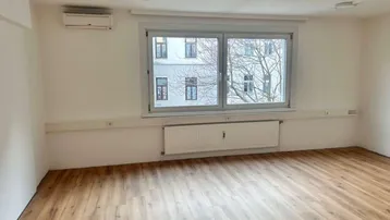Heller Büroraum mit modernem Laminatboden, großen Fenstern und Klimaanlage für angenehmes Raumklima.