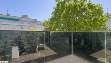 Heller Balkon mit Glasbrüstung und Blick ins Grüne sowie auf umliegende Gebäude.