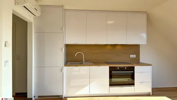 Moderne Einbauküche mit weißen Hochglanzfronten, Holzakzenten und integrierten Geräten.