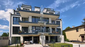 Modernes Mehrfamilienhaus mit gestuften Balkonen und Dachterrassen unter blauem Himmel.
