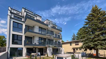 Modernes Apartmentgebäude mit mehreren Balkonen und einem kleinen Gartenbereich unter strahlend blauem Himmel.