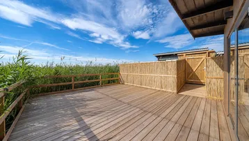 Geräumige Holzterrasse mit Bambuszaun und Blick ins Grüne unter blauem Himmel.