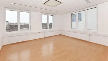 Helles und geräumiges Büro mit großen Fenstern, Klimaanlage und hellem Laminatboden, ideal für verschiedene Nutzungen.