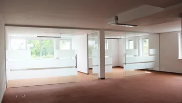 Heller Büroraum mit Teppichboden und modernen Glasabtrennungen, die natürliches Licht hereinlassen.