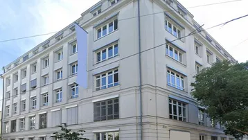 Mehrstöckiges Gebäude mit klassischer Architektur und vielen Fenstern an einer städtischen Straße.