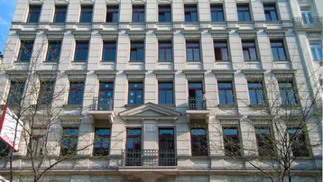 Historisches Gebäude mit weißer Stuckfassade, roten Fenstern und kleinen Balkonen in gutem Zustand.