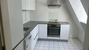 Helle Küche mit weißen Schränken, grauer Arbeitsplatte und Dachschräge, ausgestattet mit modernen Geräten.