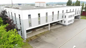 Luftaufnahme eines modernen Geschäftsgebäudes mit weiß-grauer Fassade und großem Parkplatzbereich.