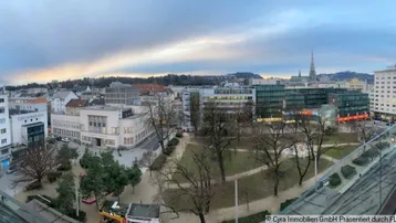 Panoramablick über die Stadt mit Gebäuden, Park und bewölktem Himmel von einer erhöhten Position.