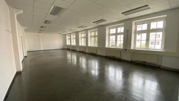 Geräumiger, heller Raum mit zahlreichen Fenstern, dunklem Boden und praktischer Rasterdecke.