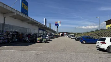 Außenansicht eines Einkaufszentrums mit großem Parkplatz und blauer Beschilderung unter klarem Himmel.