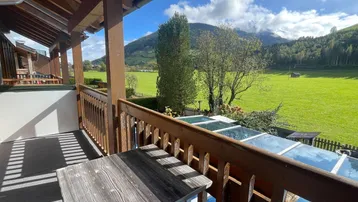 Geräumiger Balkon mit Holzboden und Geländer, bietet einen weiten Blick auf die umliegende Berglandschaft und grüne Wiesen.