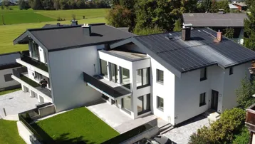 Moderne Wohnanlage mit Balkonen, privatem Gartenbereich und Bergblick in grüner Umgebung.