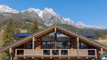 Modernes Holzchalet mit großen Glasfronten und beeindruckendem Bergblick unter blauem Himmel.