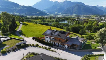Luftaufnahme eines traditionellen Gebäudes mit Solaranlage und Bergblick in grüner Landschaft.