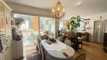 Helles Esszimmer mit Kronleuchter, Holzboden und Zugang zu einem sonnigen Balkon.