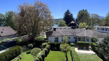 Gepflegter Gartenbereich mit Rasenflächen und Hecken, umgeben von weiteren Häusern und einem See im Hintergrund.
