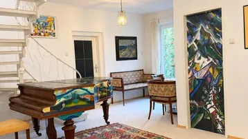 Geräumiges Wohnzimmer mit Wendeltreppe, Flügel und farbenfrohem Teppich, hell und einladend.